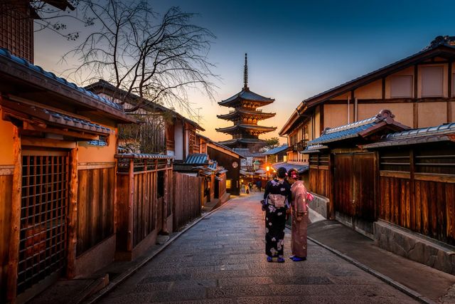 Two women in kimono on a stone lane in Higashiyama, Kyoto, with the Yasaka Pagoda at sunset